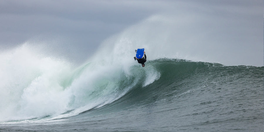 Bodyboarder tumbado sobre su tabla en una ola verde, con aletas en los pies