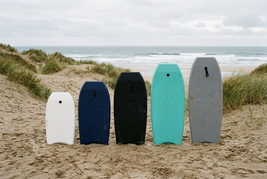 Cinq planches de bodyboard de tailles croissantes alignées debout sur le sable