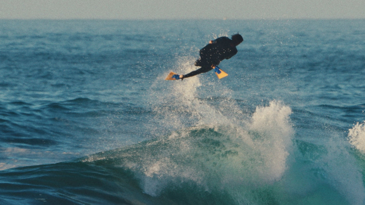 Bodyboarder tumbado sobre su tabla en una ola verde, con aletas en los pies