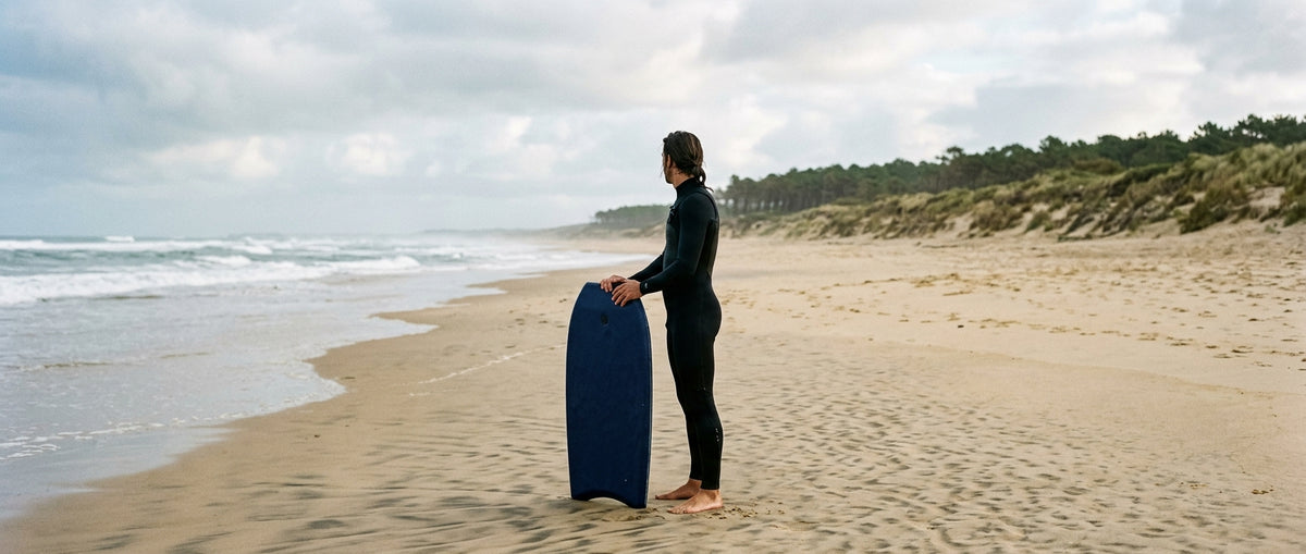 Rider mesurant sa planche de bodyboard à la verticale, talon au sol, sur la plage